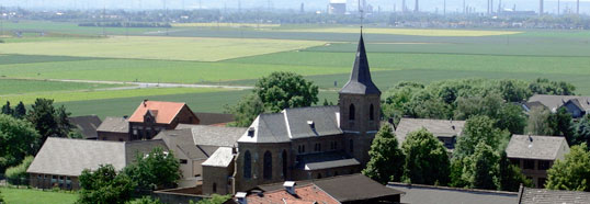 Libur im Schatten der Pfarrkirche Sankt Margaretha. Am Horizont lassen sich die auf der anderen Rheinseite liegenden, sieben Kilometer entfernten Raffinerieanlagen in Godorf und Wesseling erkennen.